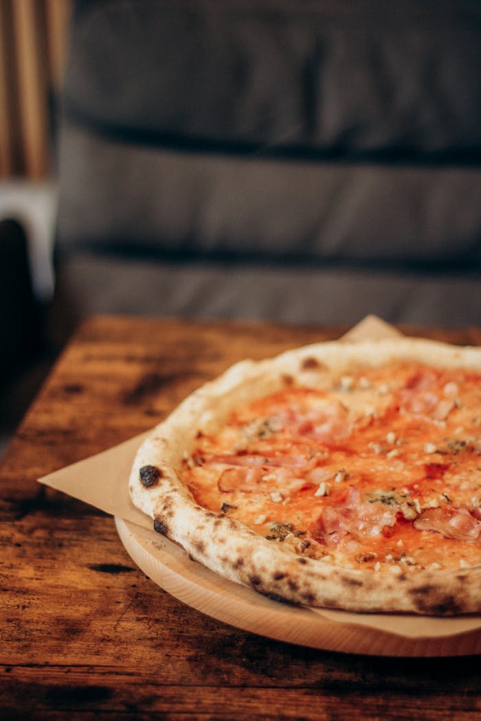 Close-up of a freshly baked Neapolitan pizza with ham on a rustic wooden table in a cozy setting.