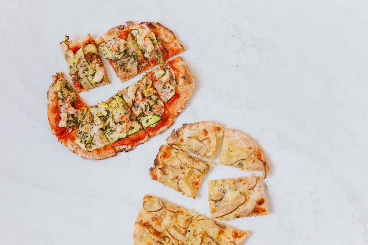Delicious gourmet pizzas with varied toppings sliced and arranged on a marble surface from a top-down perspective.