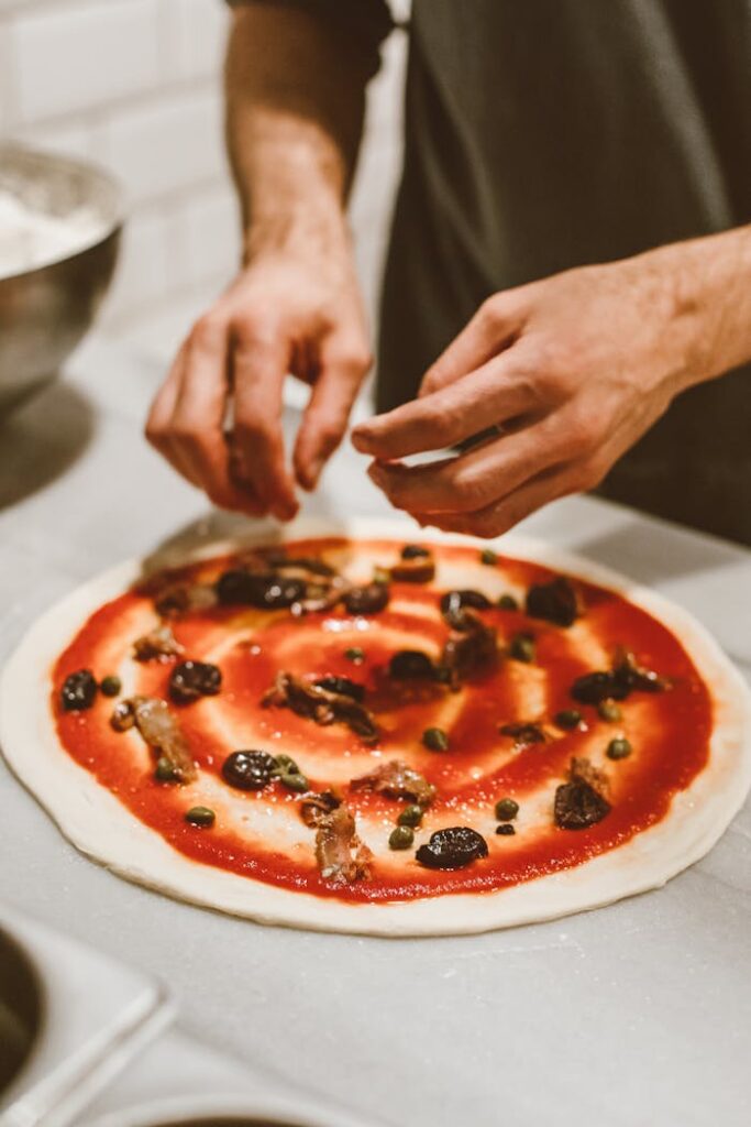 Hands expertly apply toppings to a freshly prepared artisan pizza.