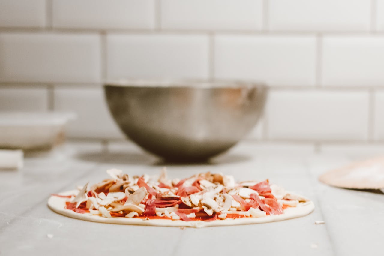Close-up of homemade pizza dough topped with fresh mushrooms and salami, ready to bake.